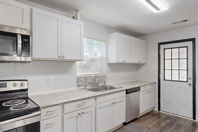 kitchen with dark wood finished floors, stainless steel appliances, visible vents, white cabinets, and a sink