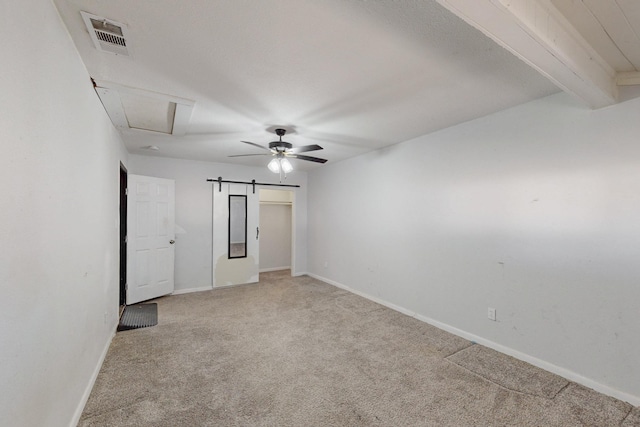 spare room featuring beam ceiling, light colored carpet, visible vents, a barn door, and baseboards