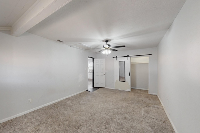 unfurnished bedroom featuring beam ceiling, light colored carpet, visible vents, a barn door, and baseboards