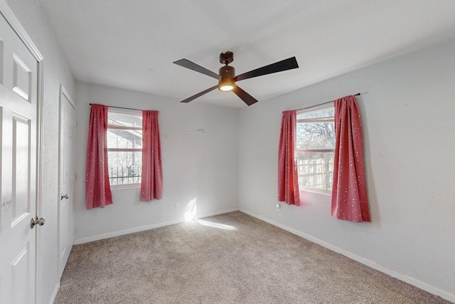 carpeted empty room featuring a wealth of natural light, ceiling fan, and baseboards