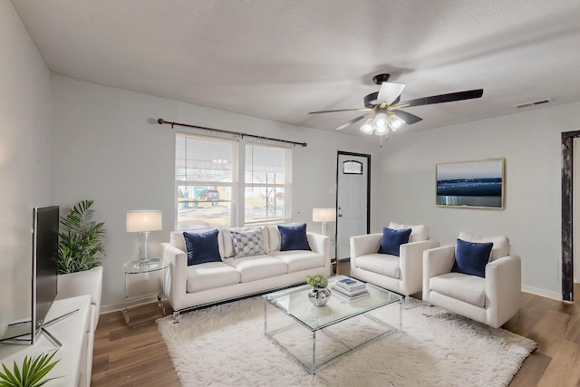 living room with a textured ceiling, ceiling fan, wood finished floors, visible vents, and baseboards