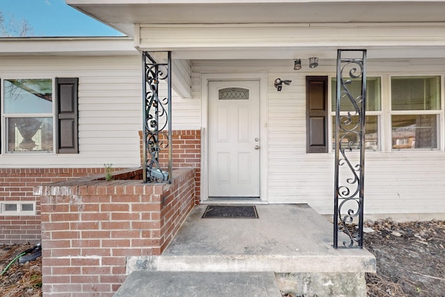 doorway to property featuring covered porch and brick siding