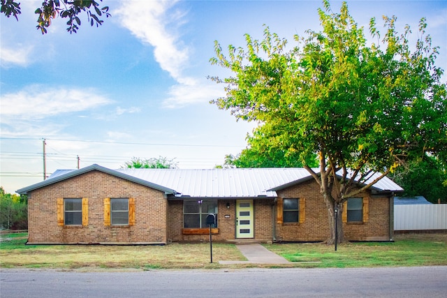 ranch-style house featuring brick siding, fence, metal roof, and a front yard