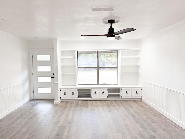 unfurnished living room with light wood-type flooring, a wainscoted wall, visible vents, and a textured ceiling