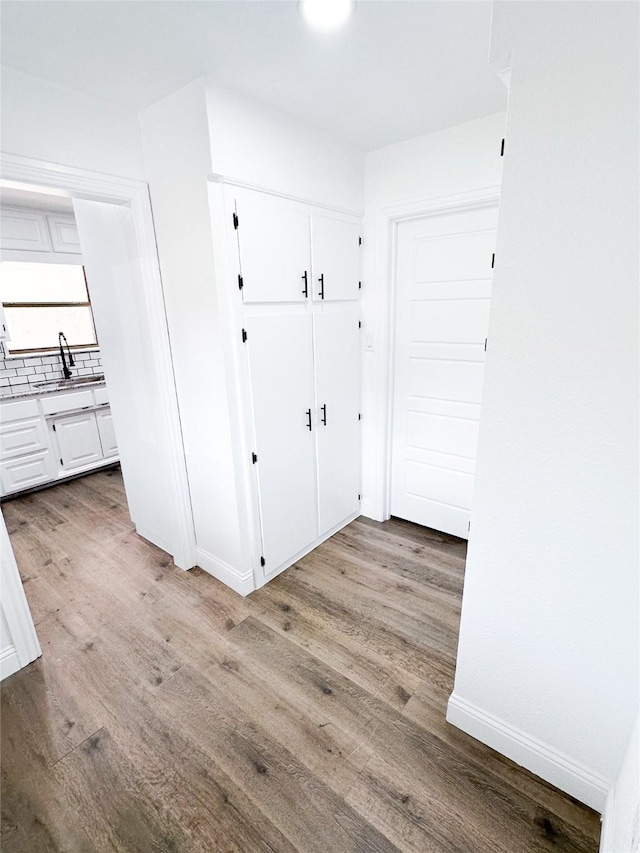 hall featuring light wood-style floors, a sink, and baseboards