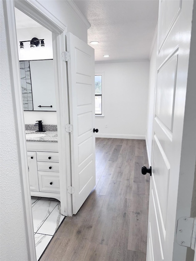 hallway featuring a sink, light wood finished floors, baseboards, and a textured ceiling