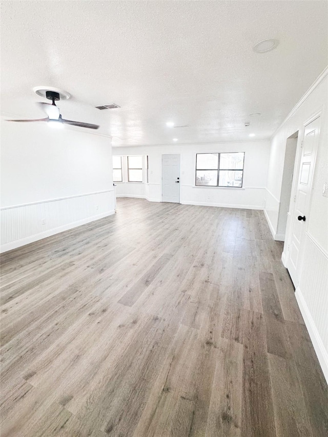 unfurnished living room with a ceiling fan, a textured ceiling, visible vents, and wood finished floors