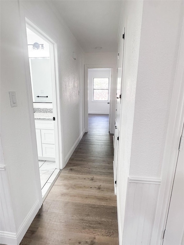 hallway with a textured wall, wainscoting, and wood finished floors