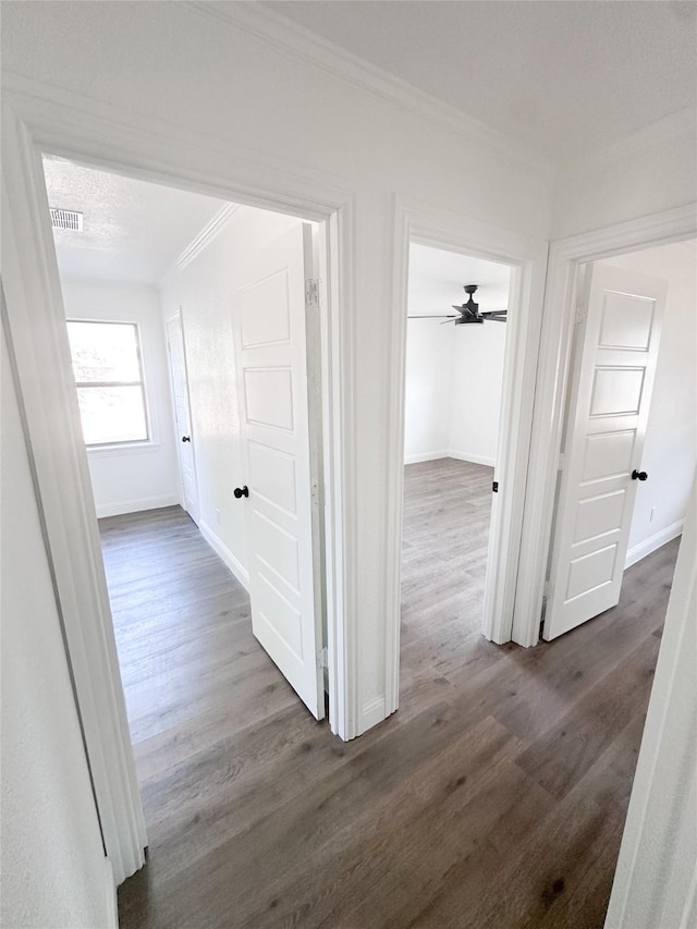 corridor featuring baseboards, dark wood-style flooring, visible vents, and crown molding