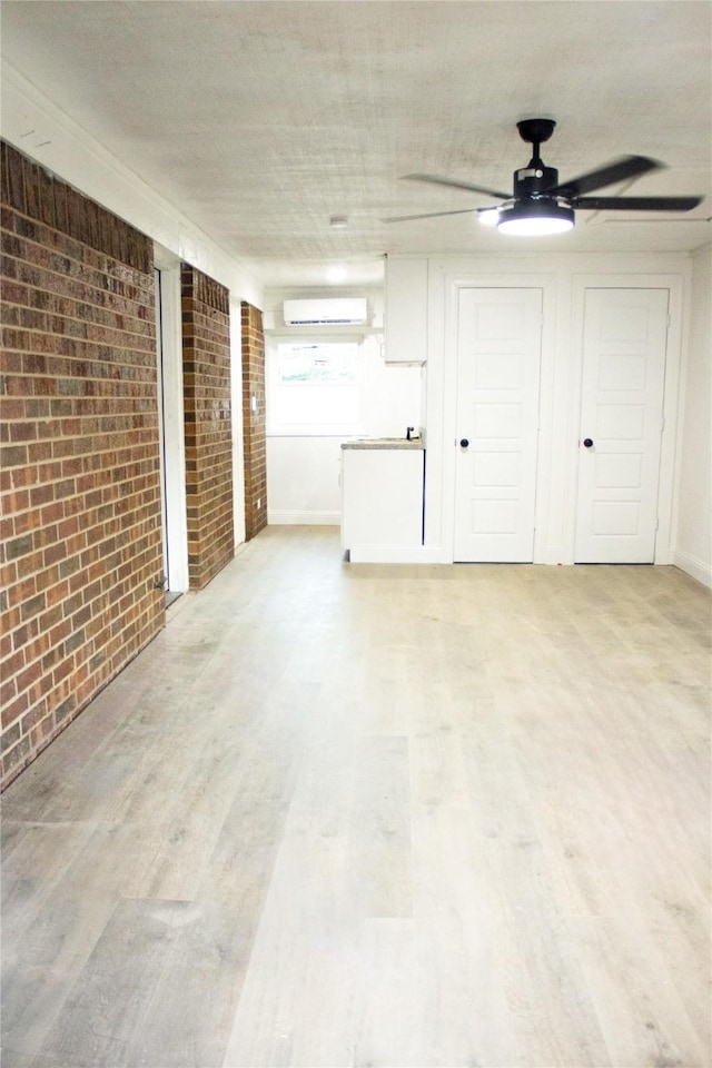 empty room with brick wall, light wood finished floors, a wall mounted air conditioner, and a ceiling fan