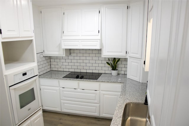 kitchen with black electric stovetop, backsplash, oven, and white cabinetry