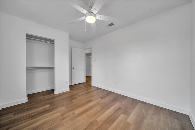 unfurnished bedroom featuring baseboards, visible vents, a ceiling fan, wood finished floors, and a closet