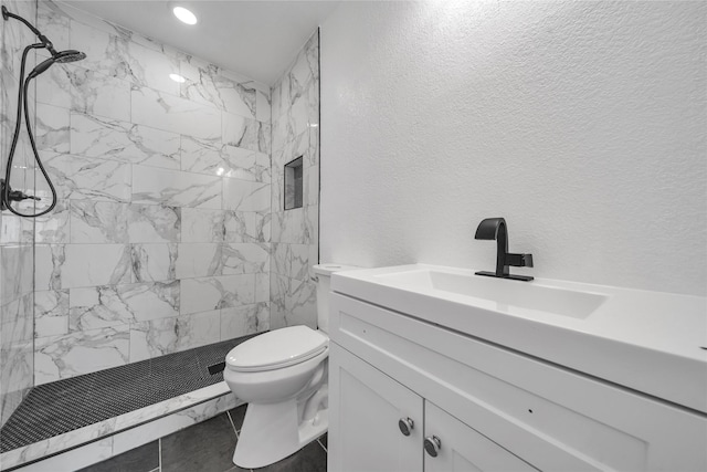 full bathroom featuring marble finish floor, a textured wall, toilet, a tile shower, and vanity