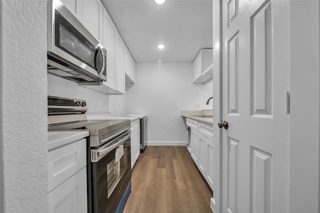 kitchen with dark wood-style floors, stainless steel appliances, light countertops, white cabinetry, and a sink