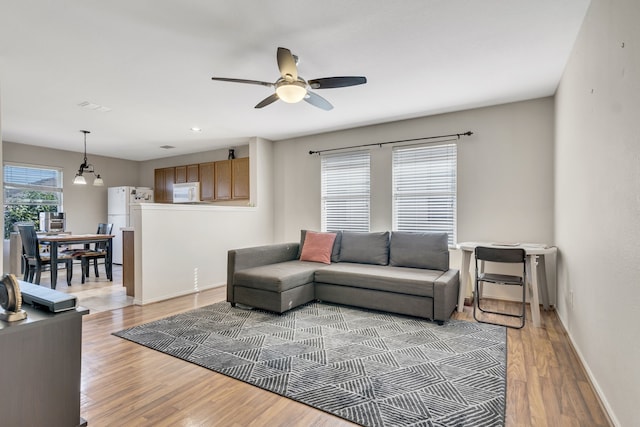 living area featuring light wood finished floors, baseboards, and a ceiling fan