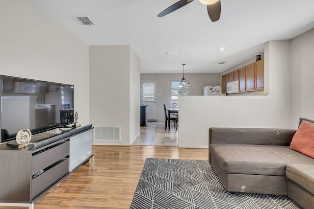 living room featuring ceiling fan, light wood-type flooring, visible vents, and baseboards