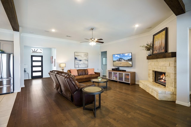 living room with a ceiling fan, dark wood-style floors, visible vents, ornamental molding, and a stone fireplace