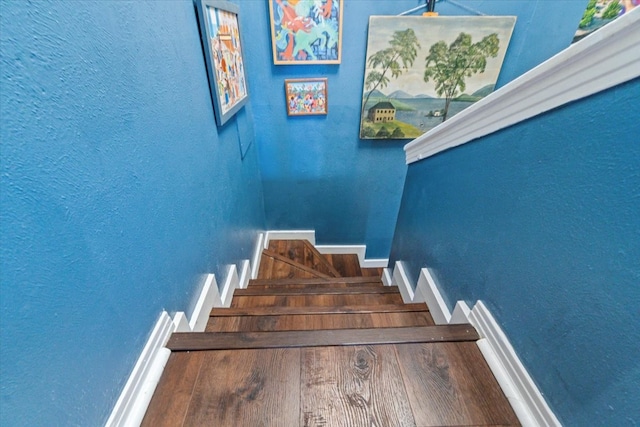 stairway featuring a textured wall, baseboards, and wood finished floors