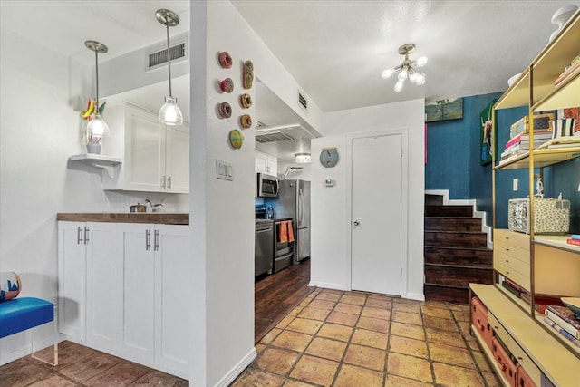 kitchen featuring appliances with stainless steel finishes, white cabinets, visible vents, and decorative light fixtures