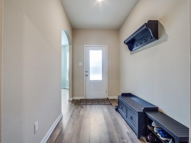 doorway featuring arched walkways, wood finished floors, and baseboards