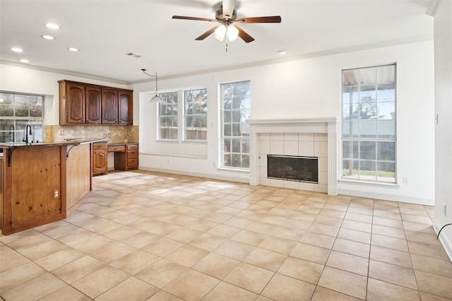 kitchen featuring decorative light fixtures, decorative backsplash, ceiling fan, a tile fireplace, and a kitchen breakfast bar