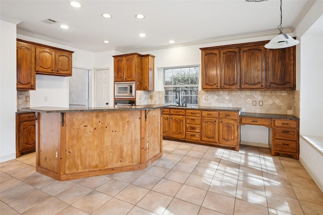 kitchen featuring visible vents, brown cabinetry, stainless steel microwave, ornamental molding, and a center island