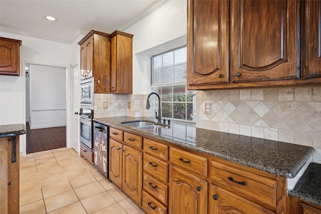 kitchen featuring light tile patterned floors, a sink, appliances with stainless steel finishes, dark stone countertops, and crown molding