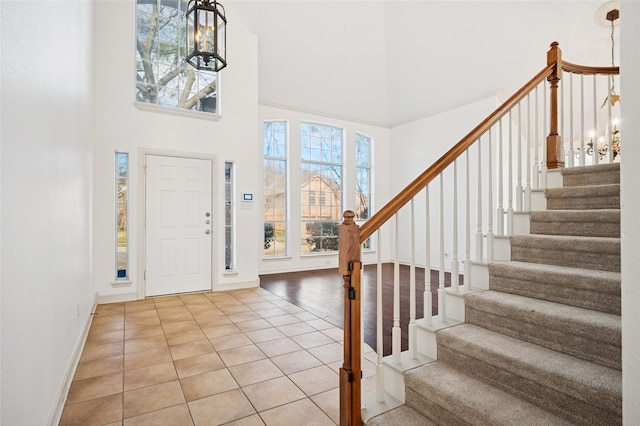 tiled foyer entrance featuring a notable chandelier, a towering ceiling, baseboards, and stairs