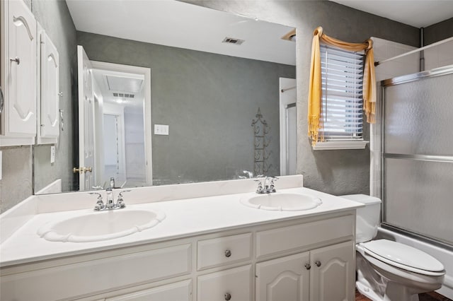 bathroom with toilet, enclosed tub / shower combo, visible vents, and a sink