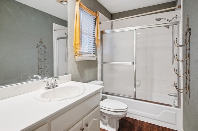 bathroom with enclosed tub / shower combo, a textured wall, toilet, wood finished floors, and vanity