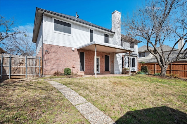 rear view of house with brick siding, a yard, a chimney, a patio, and a fenced backyard