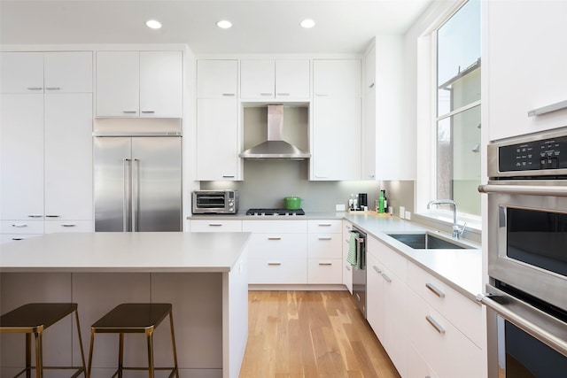 kitchen featuring a kitchen bar, plenty of natural light, stainless steel appliances, wall chimney exhaust hood, and a sink