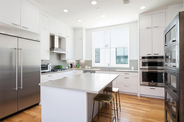 kitchen featuring a kitchen bar, light wood-type flooring, stainless steel appliances, wall chimney exhaust hood, and a sink