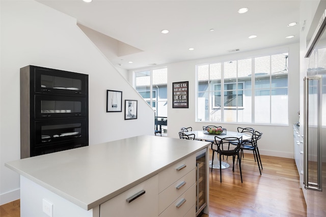 kitchen featuring a center island, beverage cooler, light countertops, recessed lighting, and light wood-style flooring