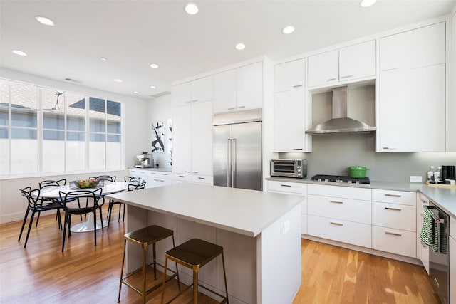 kitchen with stainless steel built in fridge, a center island, gas stovetop, a breakfast bar area, and wall chimney range hood