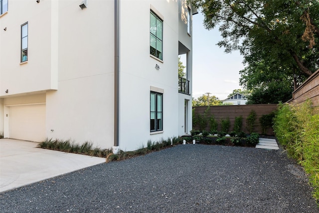 view of property exterior with concrete driveway, fence, a garage, and stucco siding