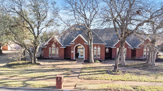 view of front facade featuring brick siding, a front yard, and a shingled roof