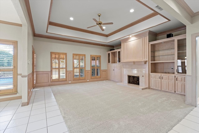 unfurnished living room with a tray ceiling, wainscoting, visible vents, and a fireplace