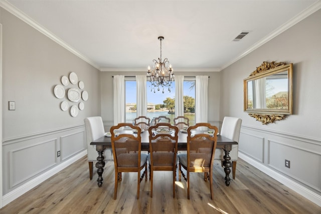 dining room featuring a notable chandelier, light wood finished floors, visible vents, and crown molding