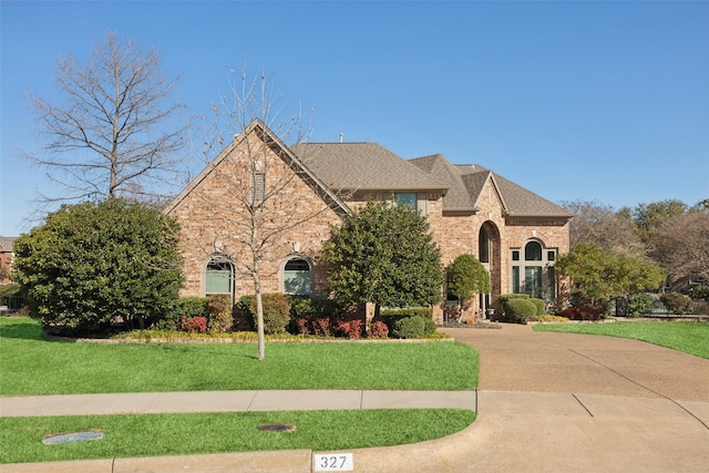 french provincial home featuring a front yard, brick siding, driveway, and roof with shingles