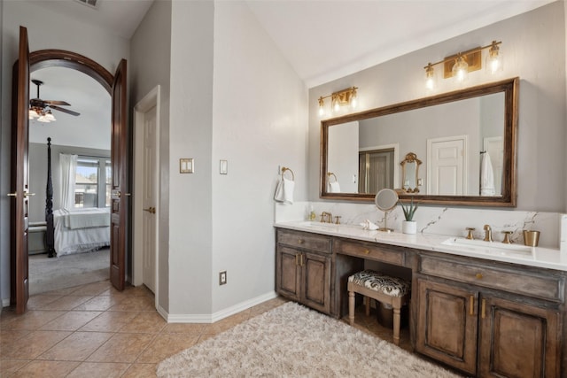 ensuite bathroom with vaulted ceiling, connected bathroom, a sink, ceiling fan, and tile patterned flooring