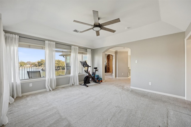 carpeted empty room with arched walkways, a raised ceiling, visible vents, and baseboards