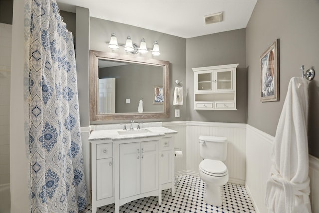 full bath featuring a wainscoted wall, curtained shower, visible vents, toilet, and vanity