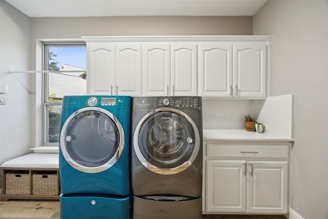 clothes washing area with cabinet space, baseboards, wood finished floors, and washing machine and clothes dryer