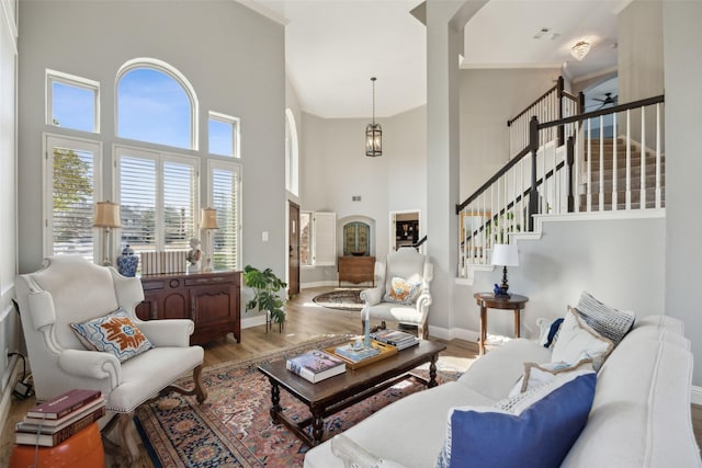 living room with stairway, a high ceiling, ornamental molding, wood finished floors, and baseboards