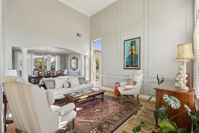 living area featuring ornate columns, arched walkways, a decorative wall, and light wood-style floors