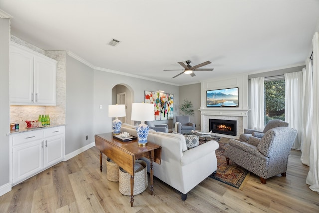 living area featuring visible vents, arched walkways, a lit fireplace, crown molding, and light wood-style floors