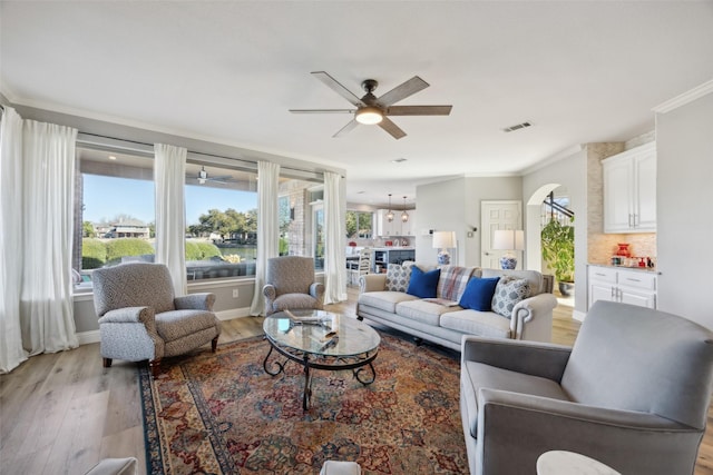 living room with visible vents, arched walkways, a ceiling fan, ornamental molding, and light wood-style floors