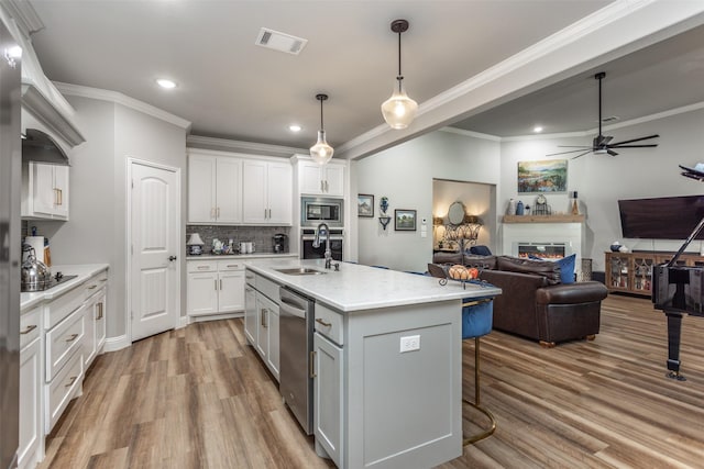 kitchen featuring stainless steel appliances, a sink, visible vents, white cabinets, and a glass covered fireplace