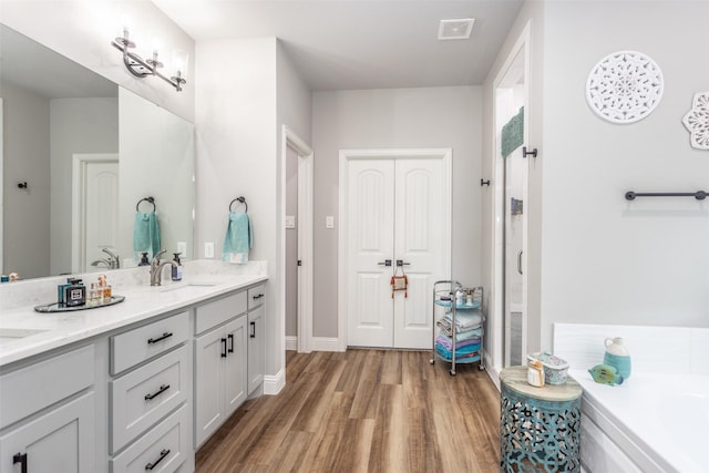 bathroom featuring visible vents, wood finished floors, a garden tub, a shower stall, and a sink